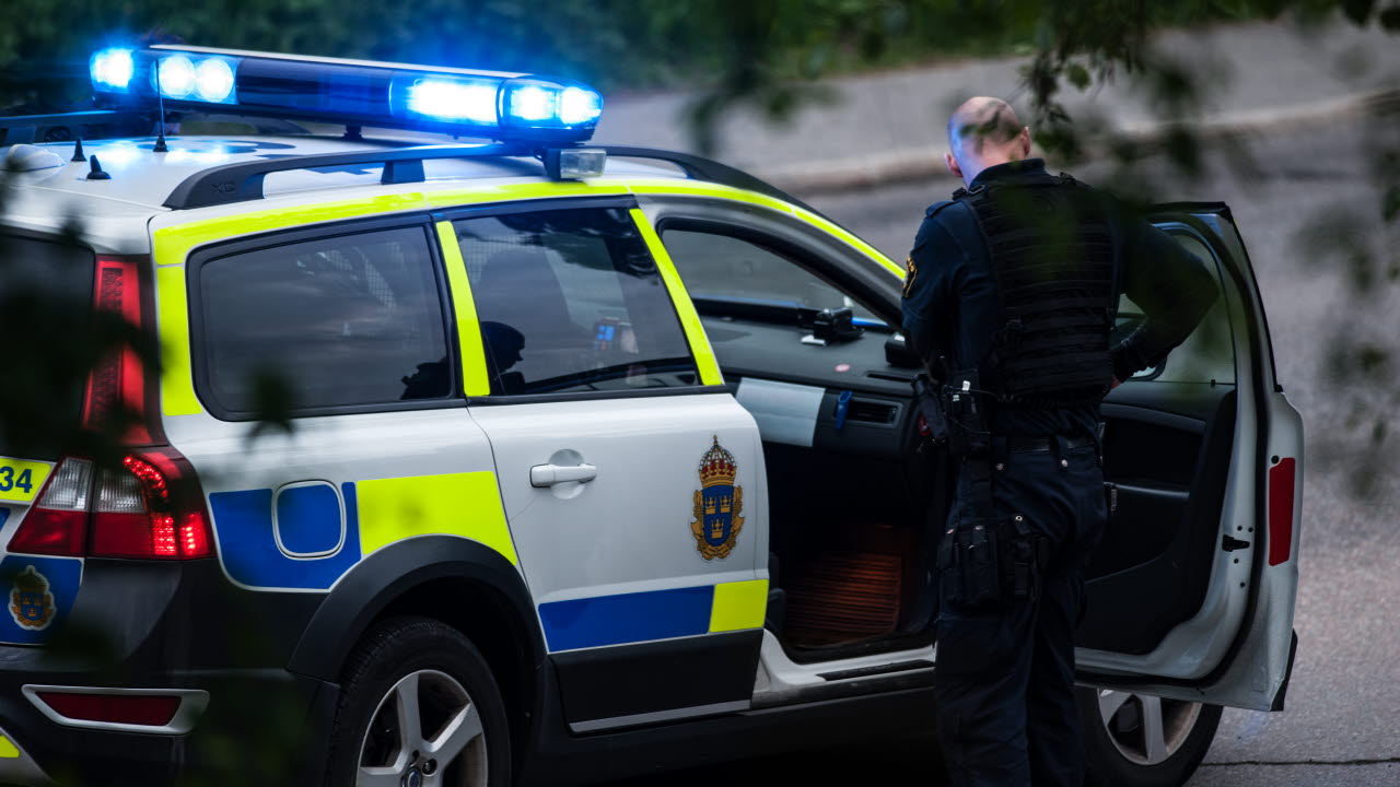 Polis utanför polisbil med blåljus på.