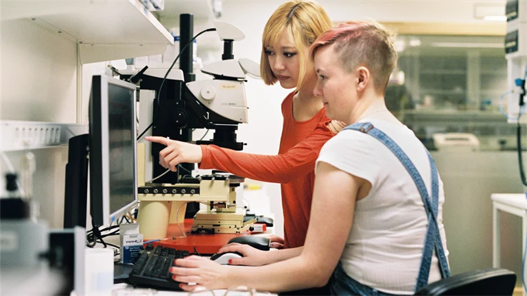Två unga personer i ett laboratorium jobbar vid en dator.
