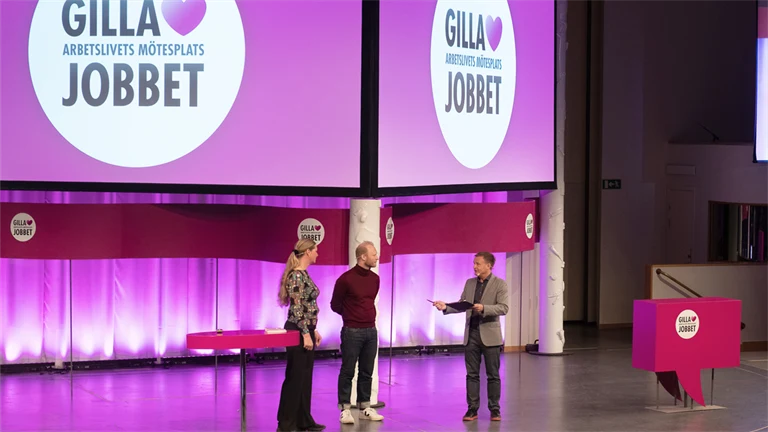 Två män och en kvinna på en stor scen inleder  arbetsmiljöeventet Gilla Jobbet 2022 i Folkets hus i Stockholm.