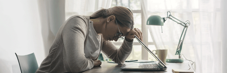 Ung kvinna sitter framför en laptop och lutar huvudet tungt framåt och blundar.