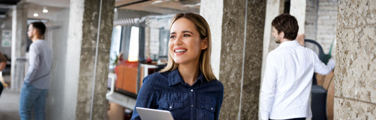 Blond, ung kvinna står upp och ler med ett kontorslandskap bakom sig.