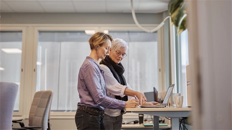 två personer sår vid ett skrivbord och jobbar med dator