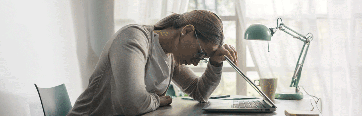 Ung kvinna sitter framför en laptop och lutar huvudet tungt framåt och blundar.