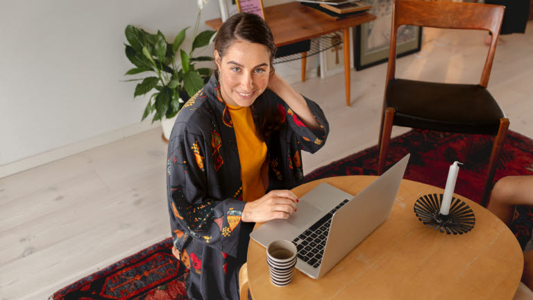 Kvinna sitter framför ett runt bord med en laptop och ett stearinljus.