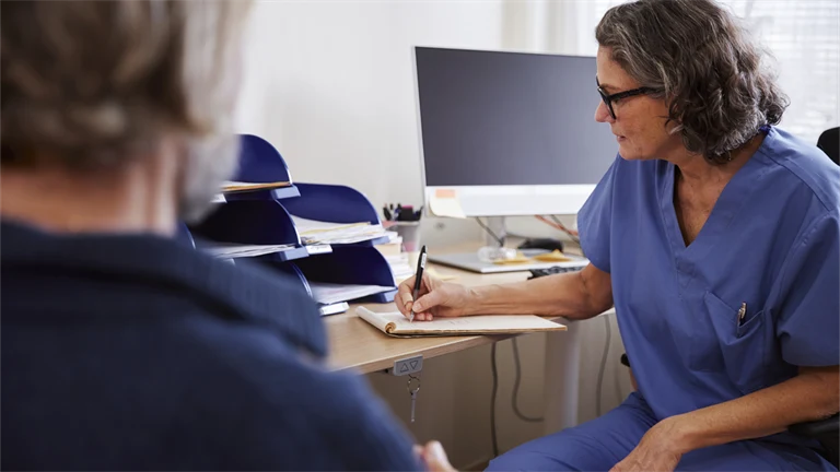 Patient på läkarbesök, där läkaren sitter och antecknar under besöket.