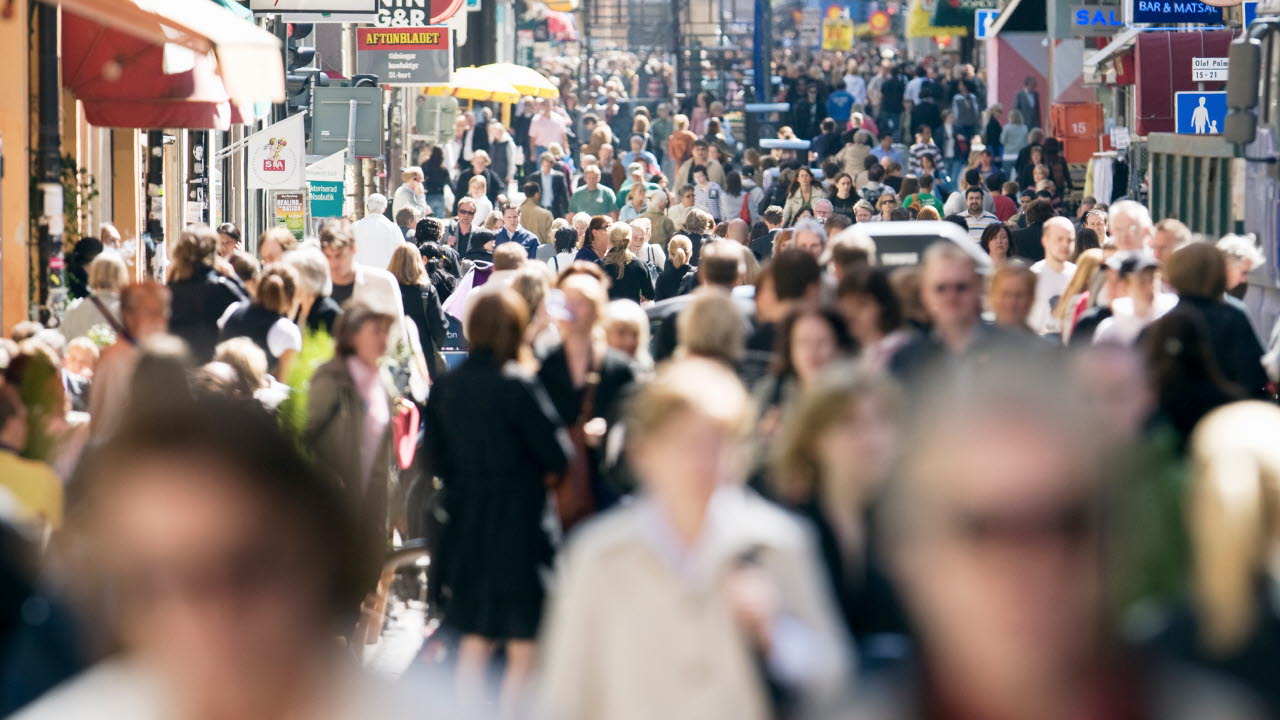 Folkträngsel på Drottninggatan, där världens nationers flaggor hänger på rader mellan husen.