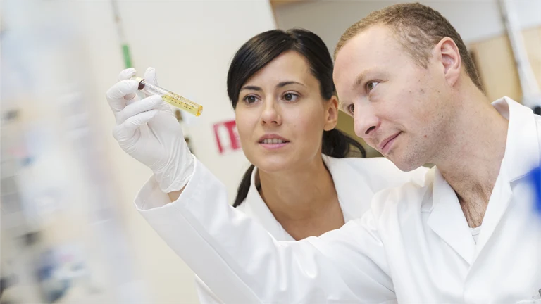 Två forskare i vita rockar tittar på ett provrör.