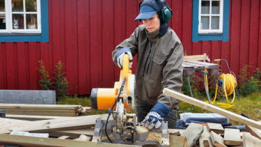 person som sågar till plankor utanför ett hus