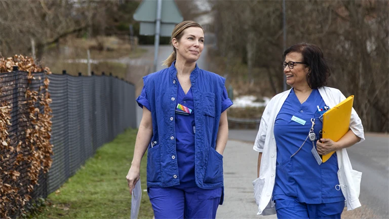 Två leende sjuksköterskor promenerar utomhus