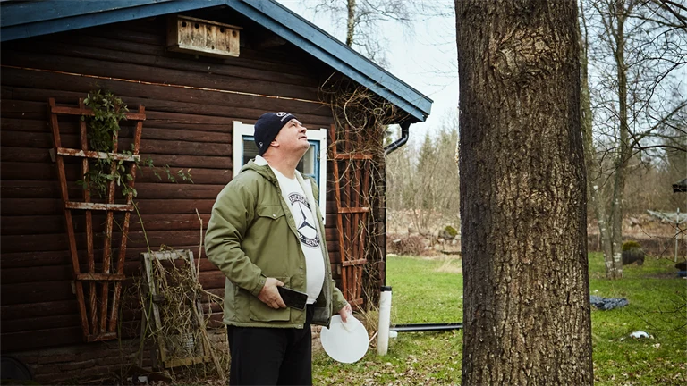 person står nedanför ett träd utanför en stuga