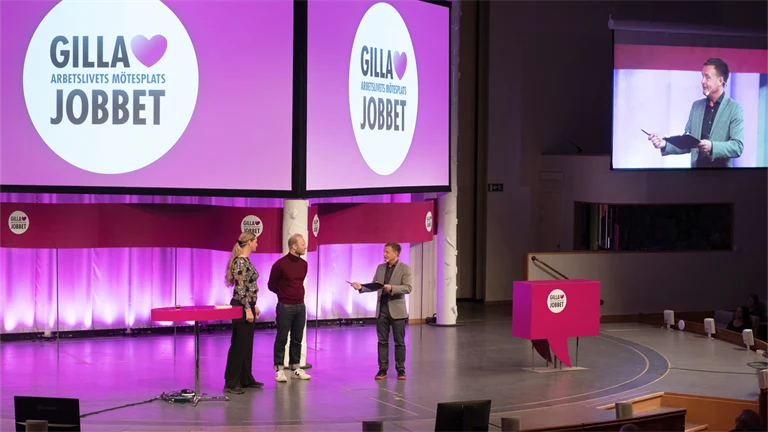 Två män och en kvinna på en stor scen inleder  arbetsmiljöeventet Gilla Jobbet 2022 i Folkets hus i Stockholm.