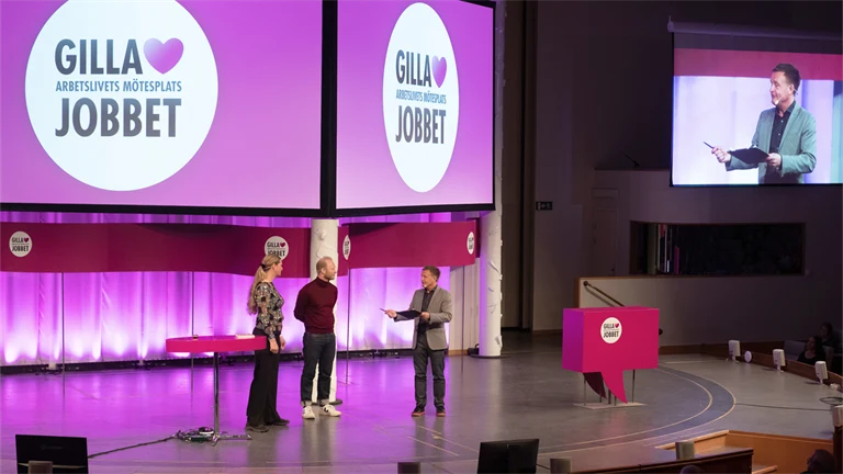 Två män och en kvinna på en stor scen inleder arbetsmiljöeventet Gilla Jobbet 2022 i Folkets hus i Stockholm.