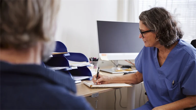 Patient på läkarbesök, där läkaren sitter och antecknar under besöket.