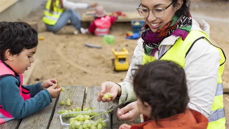 Kvinnlig förskollärare äter vindruvor med barn